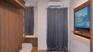A narrow room with a wooden wardrobe, a bench, a grey curtain, and a mounted TV displaying a landscape. - Cozy Studio Apartment at Sudimara Forestwalk (South Tangerang)