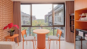 Moderni huone, jossa on suuri ikkuna, pyöreä puinen pöytä ja kaksi tuolia, pieni ruukkukasvi ja kirjahylly.