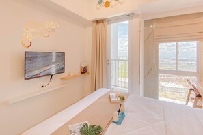 Hotelkamer met een bed, een aan de muur bevestigde televisie, een balkon met uitzicht op de stad en een raam met gordijnen.