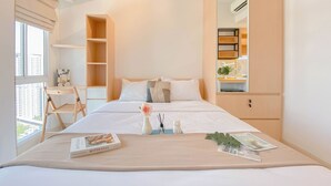 Une chambre d’hôtel avec un lit, un petit bureau, une bibliothèque et une fenêtre donnant sur des immeubles.