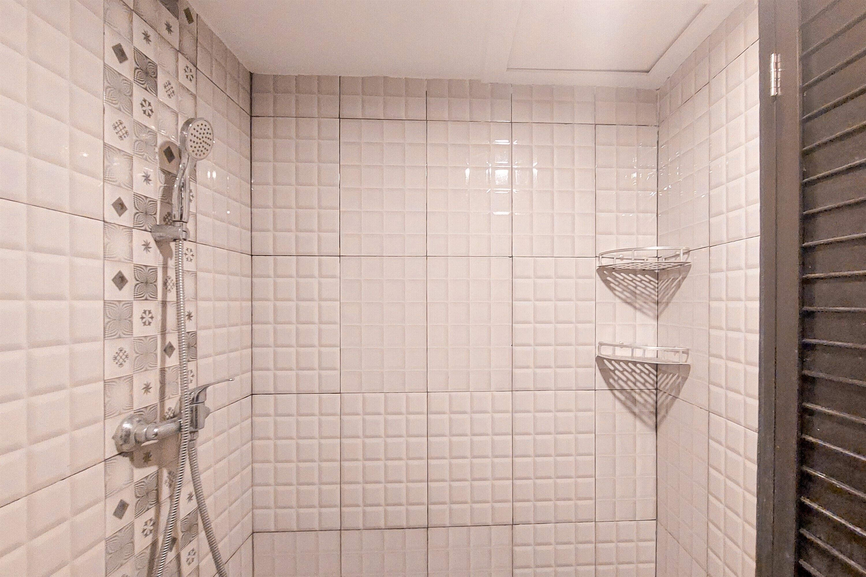 Zona de ducha con paredes de azulejos blancos, un cabezal de ducha y dos cestas metálicas.