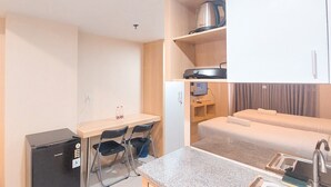 A compact hotel room with a kitchenette, a small desk with chairs, a bed with a mattress and pillows, and a built-in shower area. - Cozy and Relaxing Studio Room at De Prima Apartment (Medan)