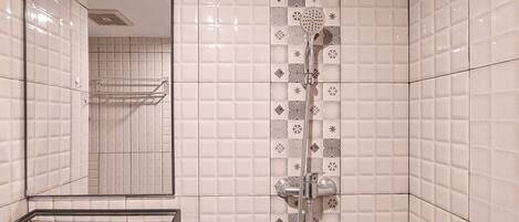 A bathroom with white tiled walls, a mirror, a shower with a handheld showerhead, and a towel rack.
