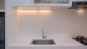 Une cuisine moderne dotée d’un évier en acier inoxydable, d’une cuisinière à gaz et de murs recouverts de carreaux blancs.