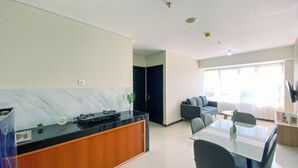 A modern kitchen with a marble backsplash, a dining area with a glass table, and a living space with a sofa and a TV.