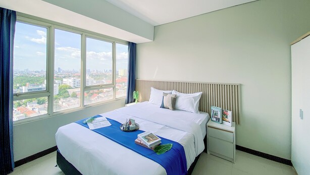 A hotel room with a large bed, a nightstand, a window with a city view, and a ceiling light.