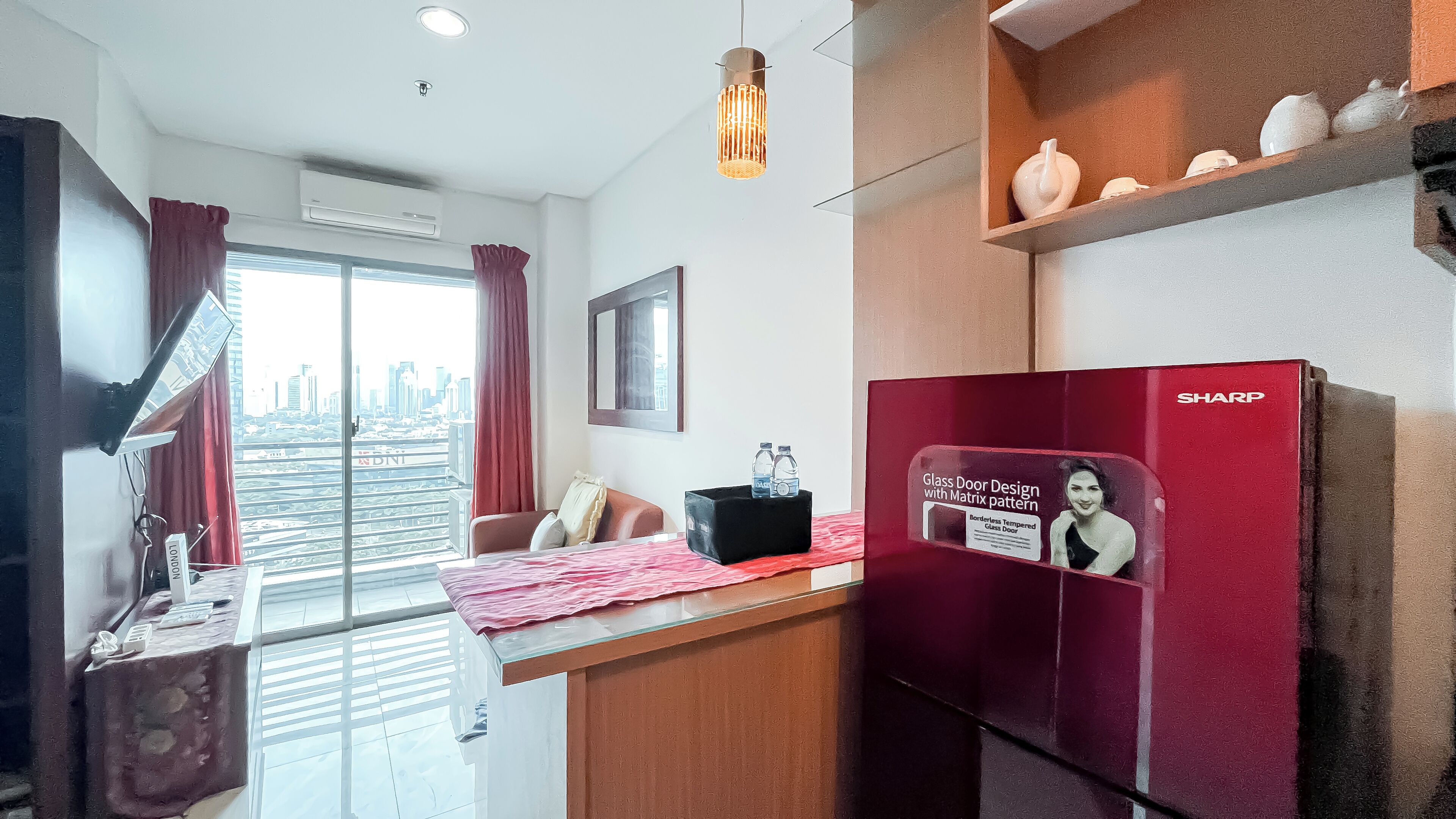 A hotel room with a bed, a desk, a refrigerator, and a window with a city view.