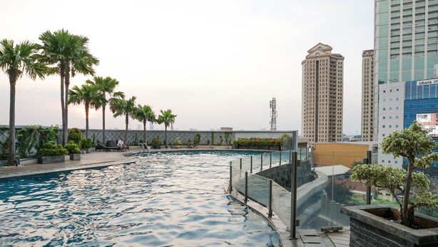 Una piscina en la azotea rodeada de palmeras y edificios modernos al fondo.