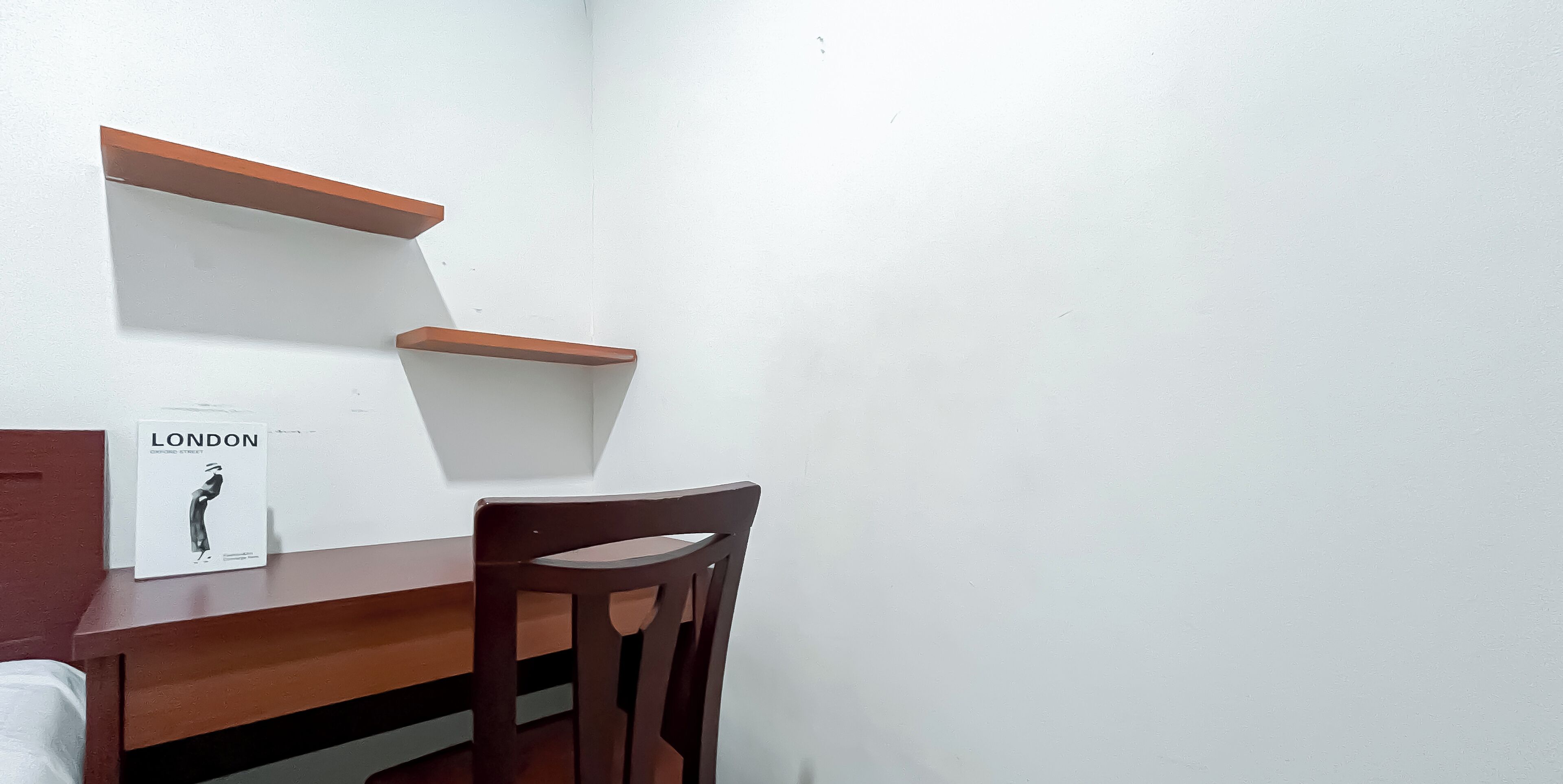 Una esquina de una habitación con un escritorio de madera, una silla y una pared blanca. Hay un cartel en la pared.