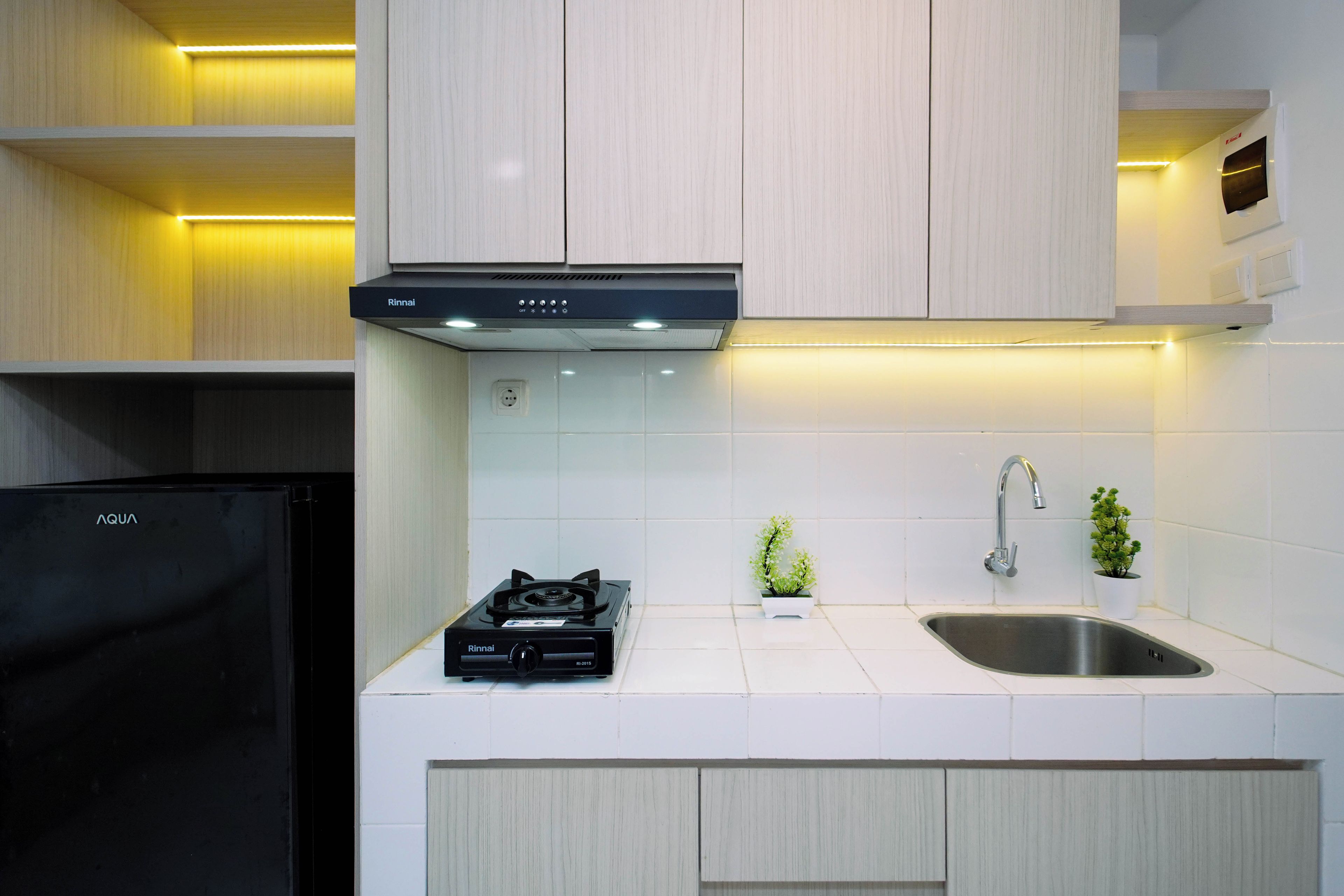 A modern kitchen with a built-in gas stove, stainless steel sink, and a compact refrigerator.