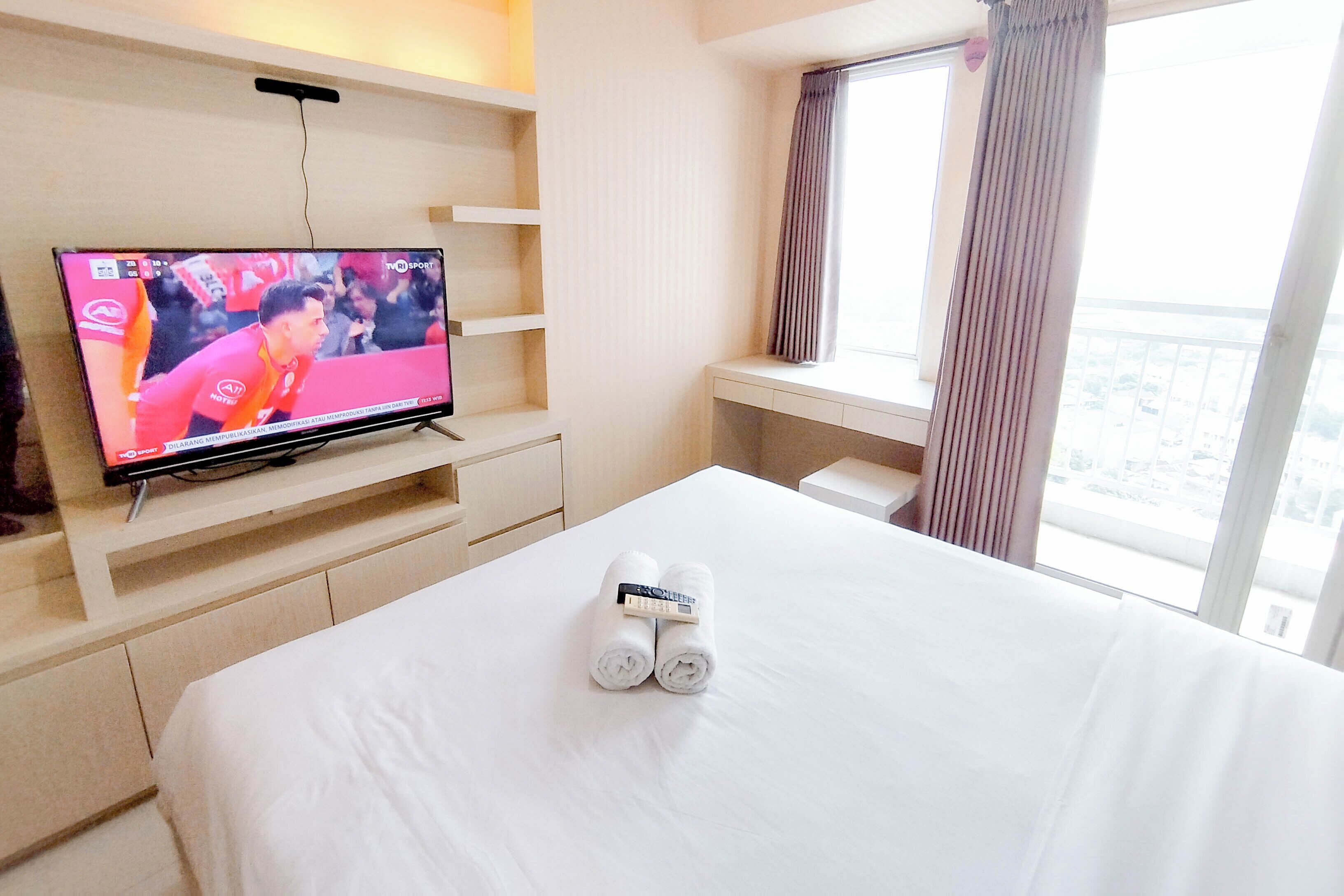 Habitació d'hotel amb un llit, una televisió sobre un suport, una finestra amb cortines i vista a la ciutat.
