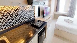 Une chambre d’hôtel moderne dotée d’un coin cuisine, d’un téléviseur à écran plat et d’un lit recouvert d’une couette blanche.