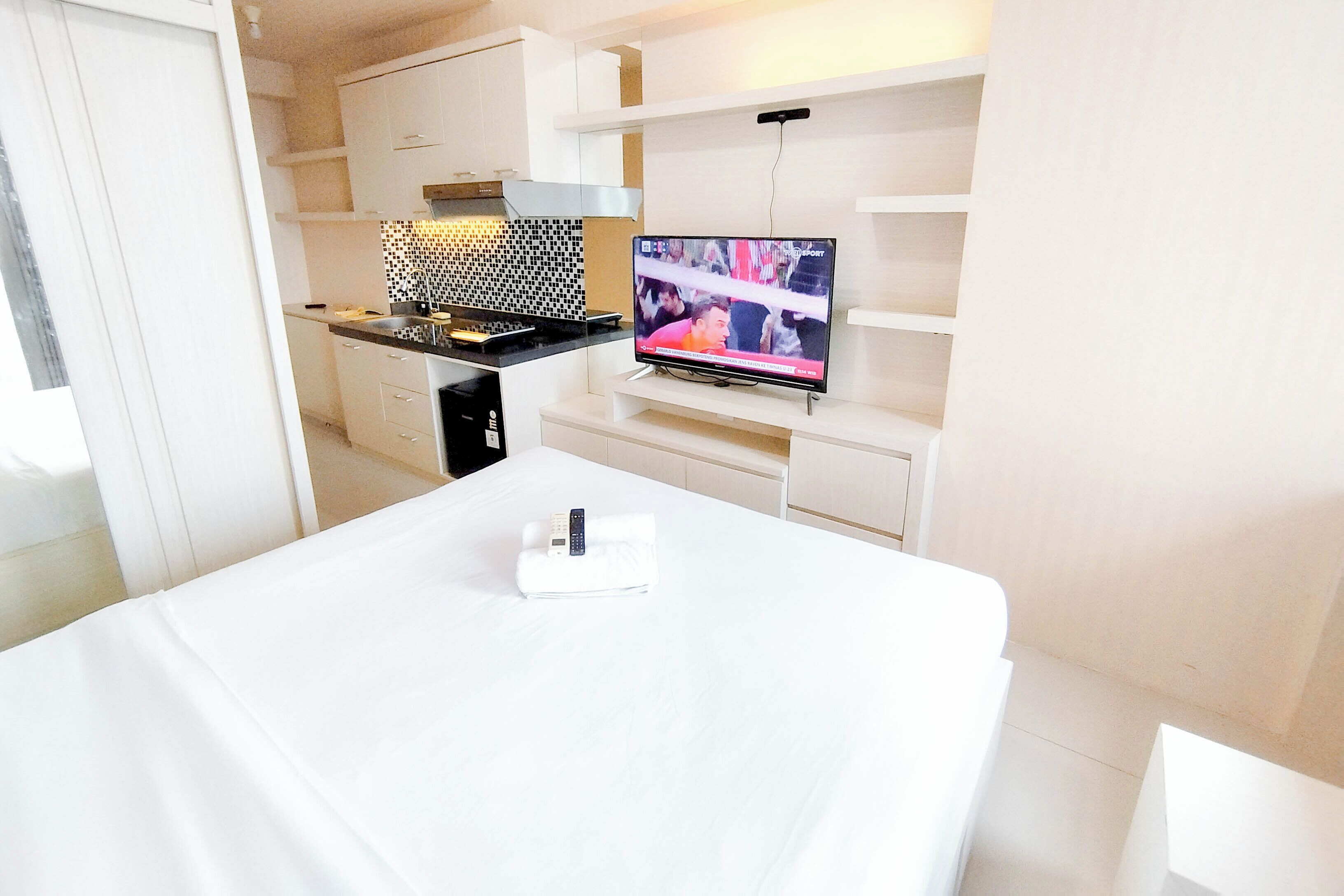 A modern hotel room with a kitchenette, a flat-screen TV, and a neatly made bed.