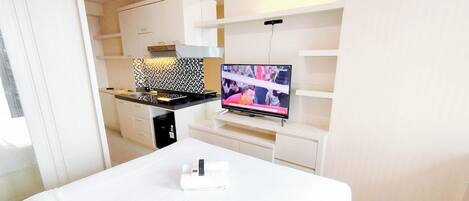 Ein modernes Hotelzimmer mit Küchenzeile, einem Flachbildfernseher und einem ordentlich bezogenen Bett.