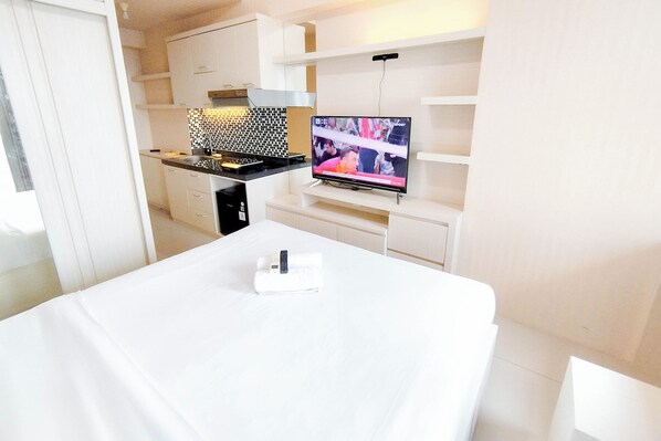 Une chambre d’hôtel moderne équipée d’une kitchenette, d’un téléviseur à écran plat et d’un lit parfaitement fait.