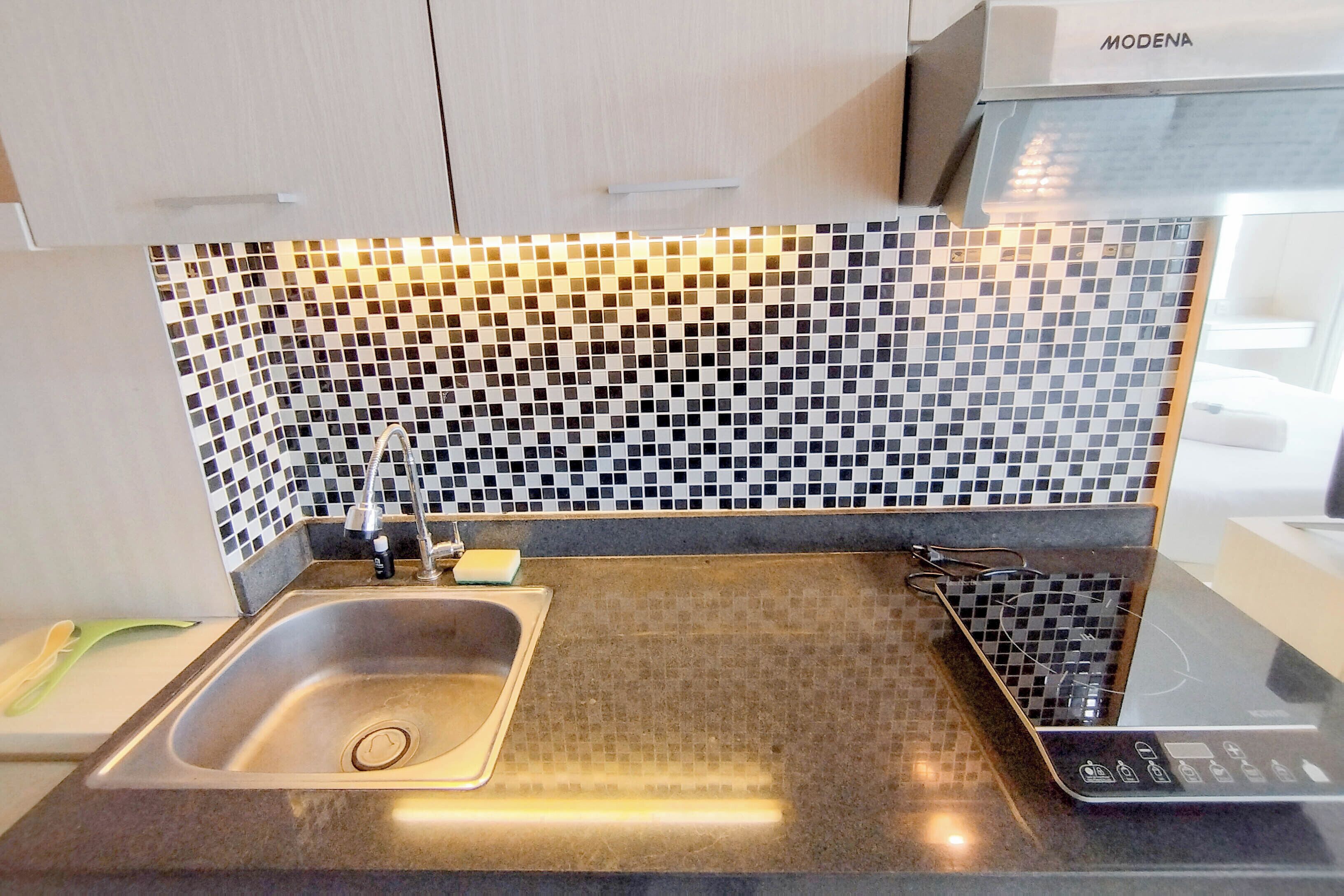 A kitchen with a stainless steel sink, a black and white tiled backsplash, and a modern induction cooktop.