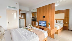 A hotel room with a large bed, a TV, a mirror, and a kitchenette. - Nice and Cozy Studio at Bogor Valley Apartment (Bogor)