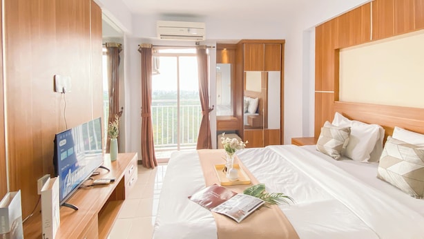 A hotel room with a bed, a TV, a desk, and a balcony with curtains. - Nice and Cozy Studio at Bogor Valley Apartment (Bogor)