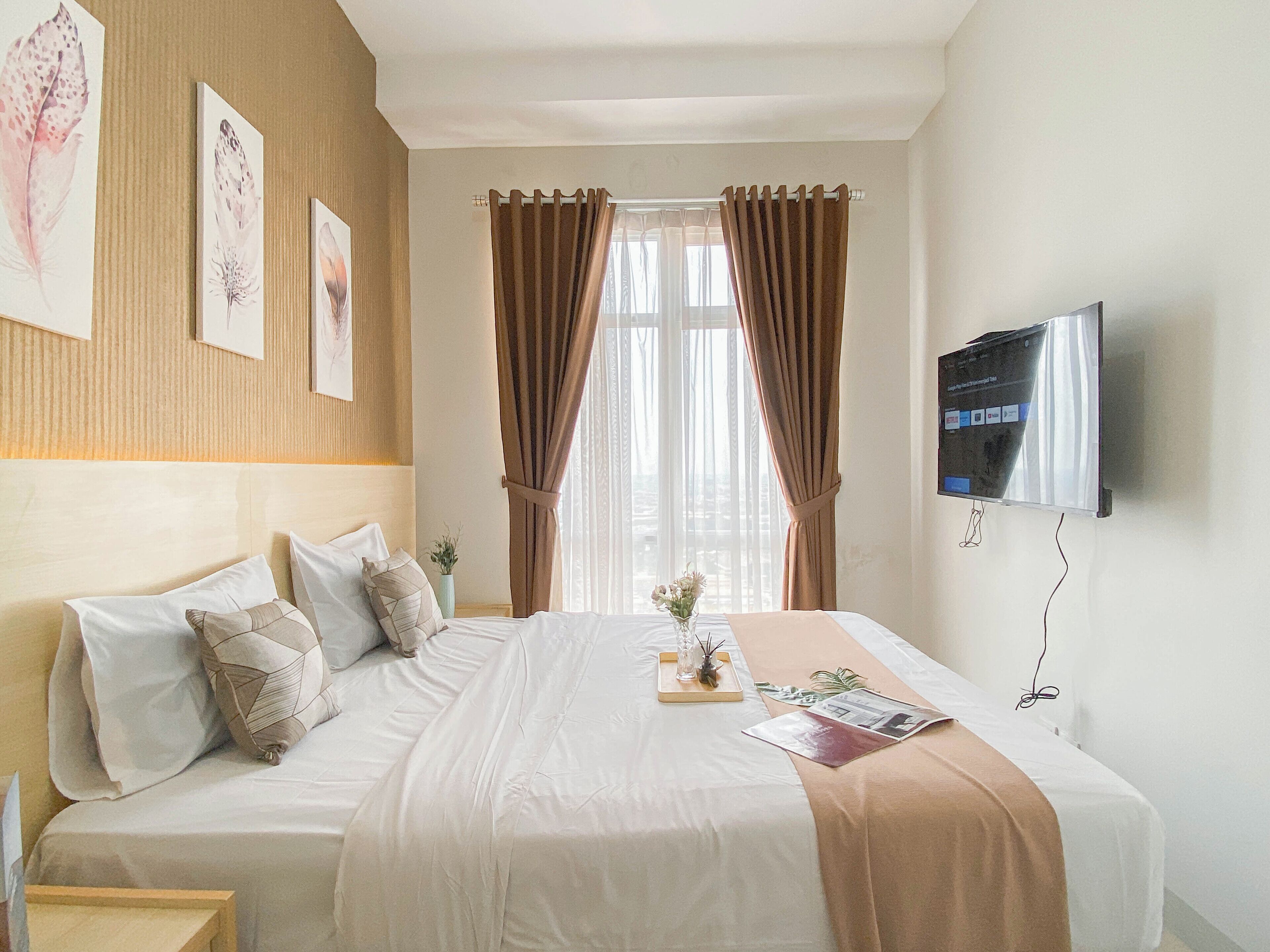 A hotel room with a bed, a TV, and a window with curtains.