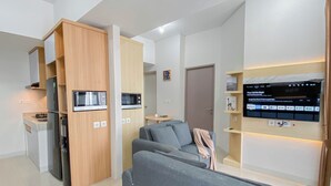 Ein modernes Wohnzimmer mit grauem Sofa, einem an der Wand montierten Flachbildfernseher und einer Küchenzeile mit integrierten Geräten.