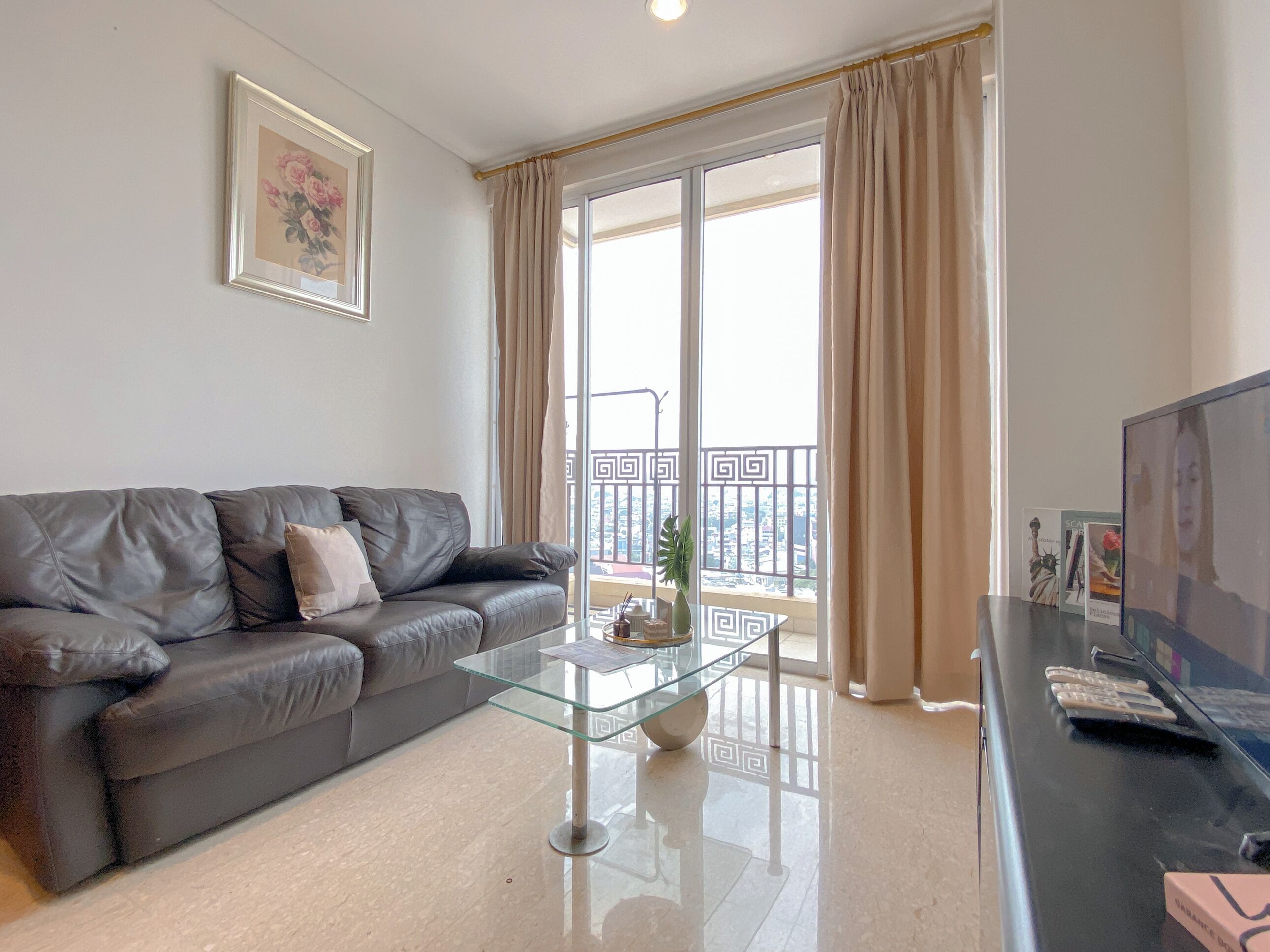 A modern living room with a leather sofa, a glass coffee table, and a large window with curtains.
