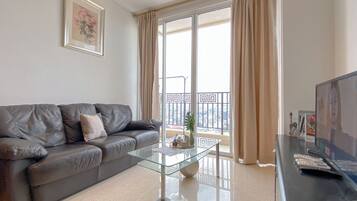A modern living room with a leather sofa, a glass coffee table, and a large window with curtains.