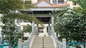 A hotel entrance with a staircase leading to a covered area, surrounded by palm trees and a pool. - Big and Cozy 3BR Apartment Lucky Tower Residence (Jakarta)