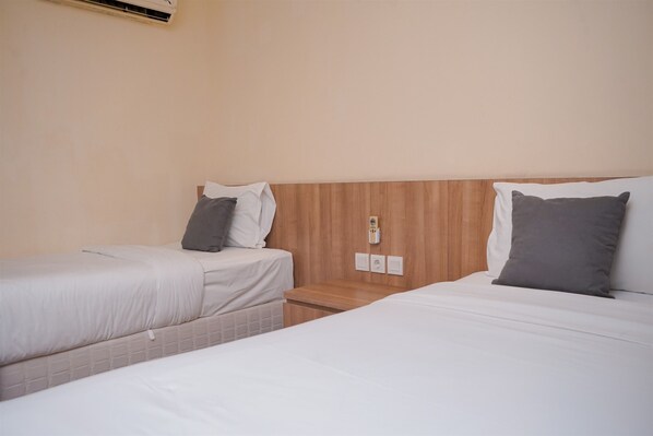 A hotel room with two single beds, each with a pillow and a nightstand.