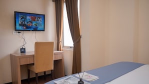 A hotel room with a bed, a desk, a chair, a television mounted on the wall, and a window with curtains.