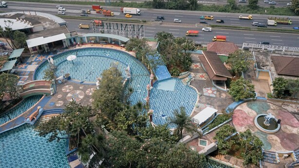 A large outdoor swimming pool with multiple lanes, surrounded by trees and a parking area.