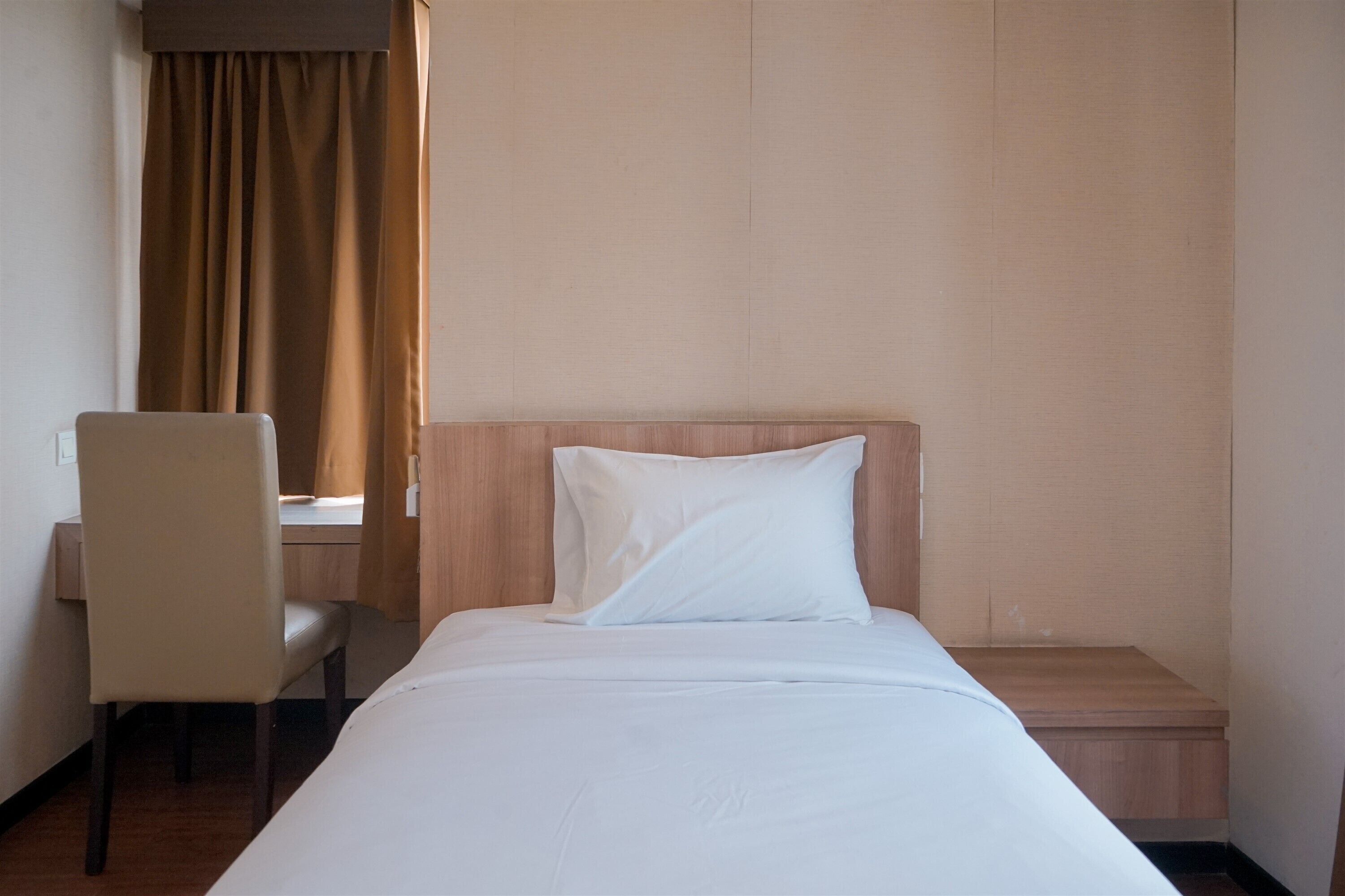 A hotel room with a bed, a chair, a desk, and a window with curtains.