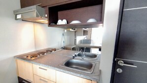 A kitchen with a double sink, a stove, and wooden cabinets. - Modern Cozy Studio at The Square Surabaya Apartment (Surabaya)