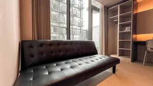 Una sala moderna con un sofá de cuero marrón oscuro, un ventanal con vista a un edificio y una estantería empotrada con una lámpara.