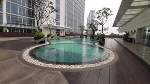 Una piscina interior moderna con borde de piedras, rodeada por una terraza de madera y plantas en macetas.