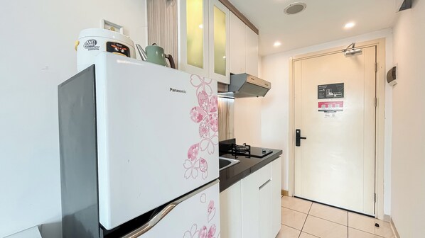 A compact kitchen with a white refrigerator, a gas stove, and a white door with a sign.