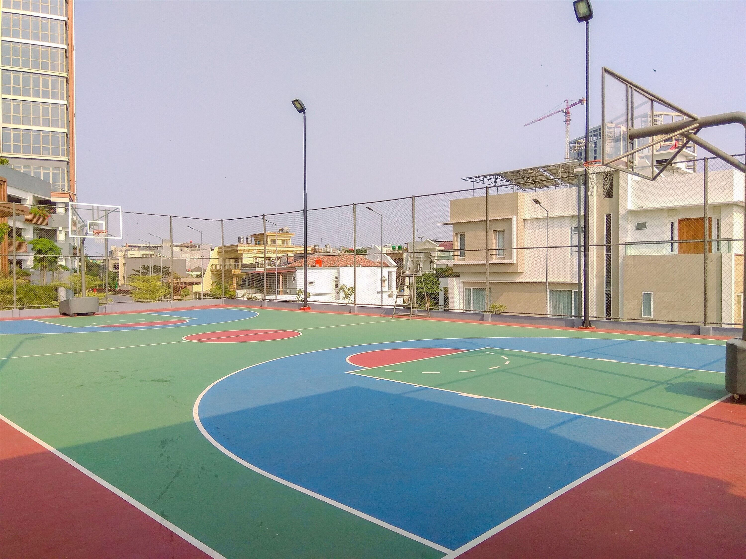 Un terrain de basket-ball en plein air, équipé d’un panier de basket et entouré d’une clôture en treillis métallique.