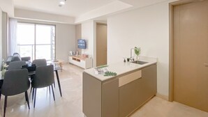 A modern kitchen with a central island, a dining area with a table and chairs, and a TV mounted on the wall. - Fully Furnished and Elegant 2BR at Gold Coast Apartment PIK (Jakarta)