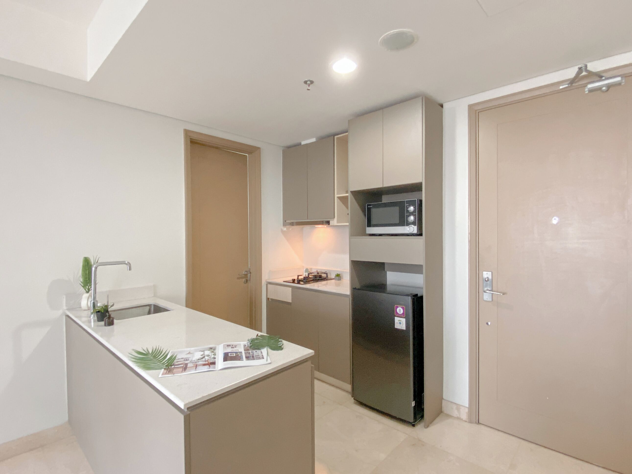 A compact kitchen with a built-in microwave, a refrigerator, and a small island with a sink and decorative items.