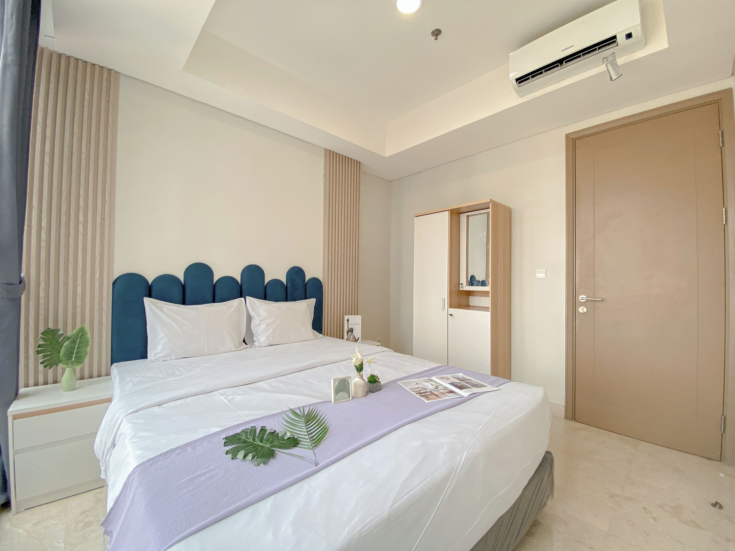 A modern bedroom with a large bed, a bedside table, a nightstand, a wardrobe, a mirror, and an air conditioning unit.