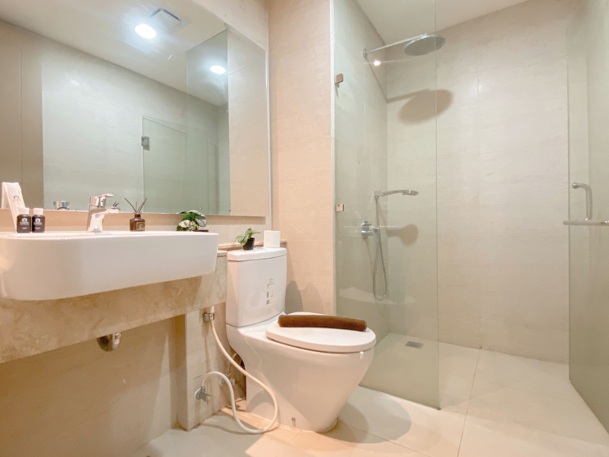 Un baño moderno con ducha de vidrio, inodoro blanco y lavamanos con artículos de tocador.