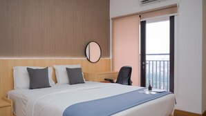 A hotel room with a bed, bedside table, chair, and a view of the city through the window. - Cozy Studio at Atria Residence Gading Serpong Apartment (Gading Serpong)