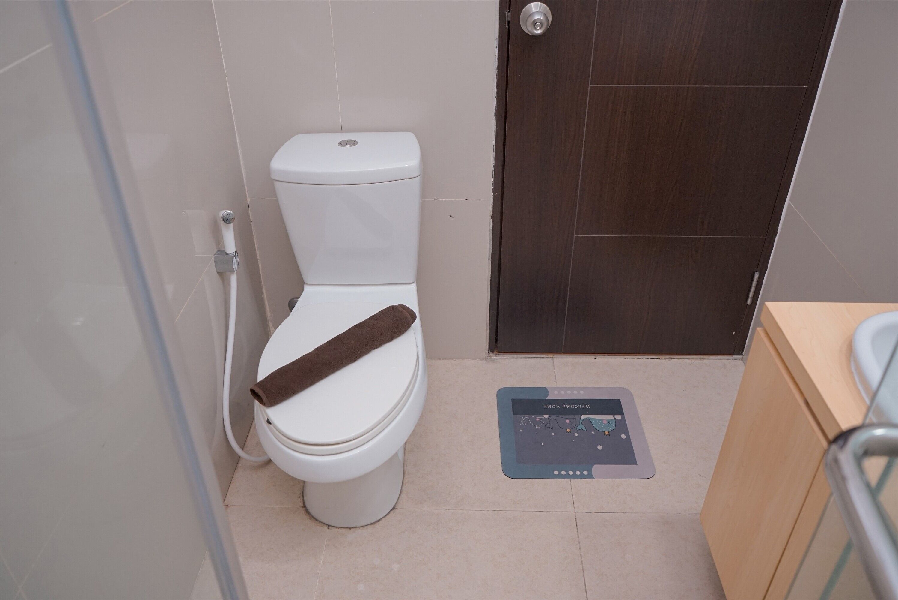 A toilet with a brown towel on the seat, a flush handle, and a door with a dark wood finish.