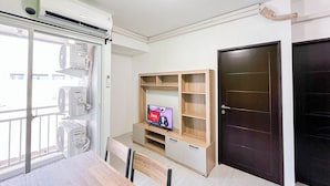 Una habitación moderna con zona de comedor, un televisor sobre un soporte de madera y una puerta oscura.
