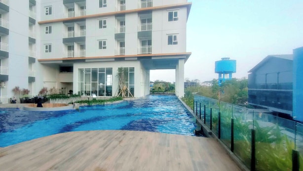 Un edificio moderno con varios balcones, una piscina y una torre de agua al fondo.
