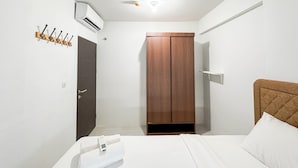 A hotel room with a bed, a wooden wardrobe, a coat rack, and an air conditioning unit.