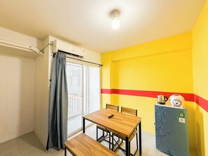 A small room with a table and chairs, a window with curtains, a radiator, and a refrigerator. - Modern and Cozy 2BR Apartment at Suncity Residence (Sidoarjo)