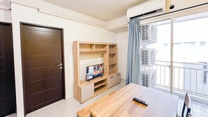 A room with a wooden table, a TV on a wooden stand, a door, and an air conditioning unit.