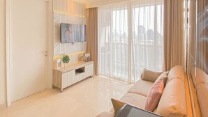 Un salon moderne avec un canapé, un téléviseur fixé au mur, une console ornée d’objets décoratifs et de grandes fenêtres avec des rideaux légers.