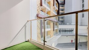 Un bâtiment moderne doté d’un balcon en verre, d’un escalier et d’un espace recouvert d’une pelouse artificielle.