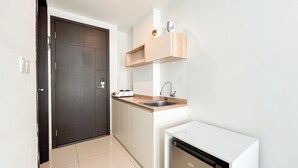 A compact kitchen with a dark door, a sink, a small countertop, and a compact refrigerator.